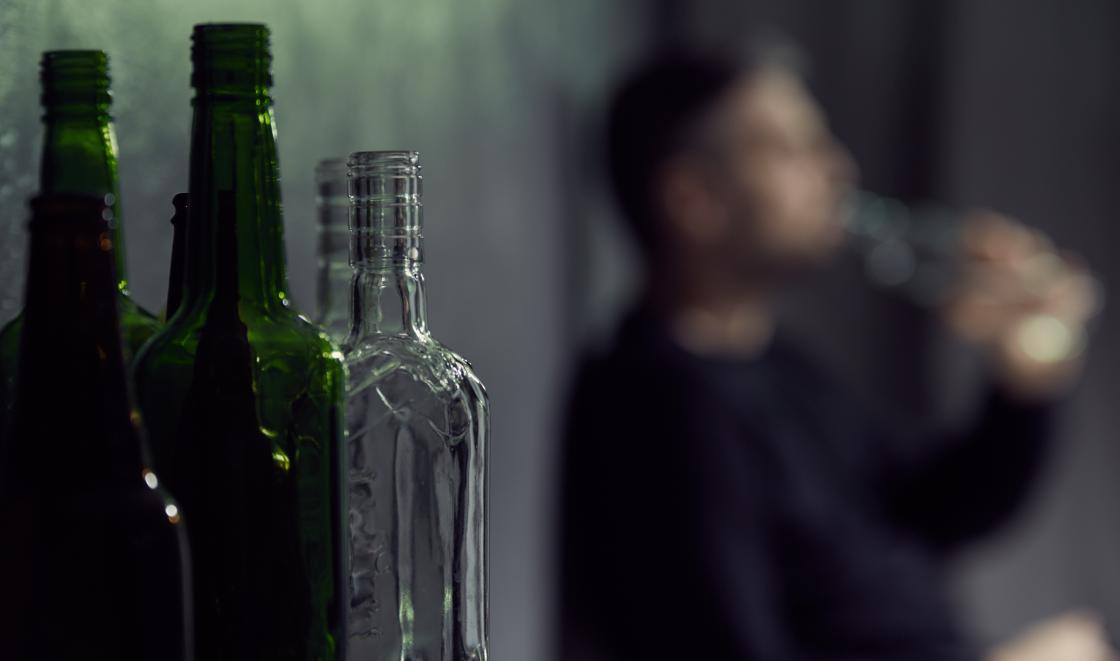 Man drinking alcohol with bottles in foreground
