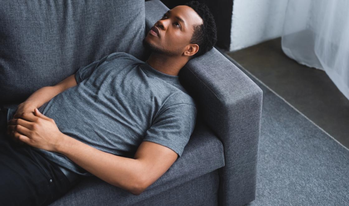 Black man laying on sofa looking at the ceiling