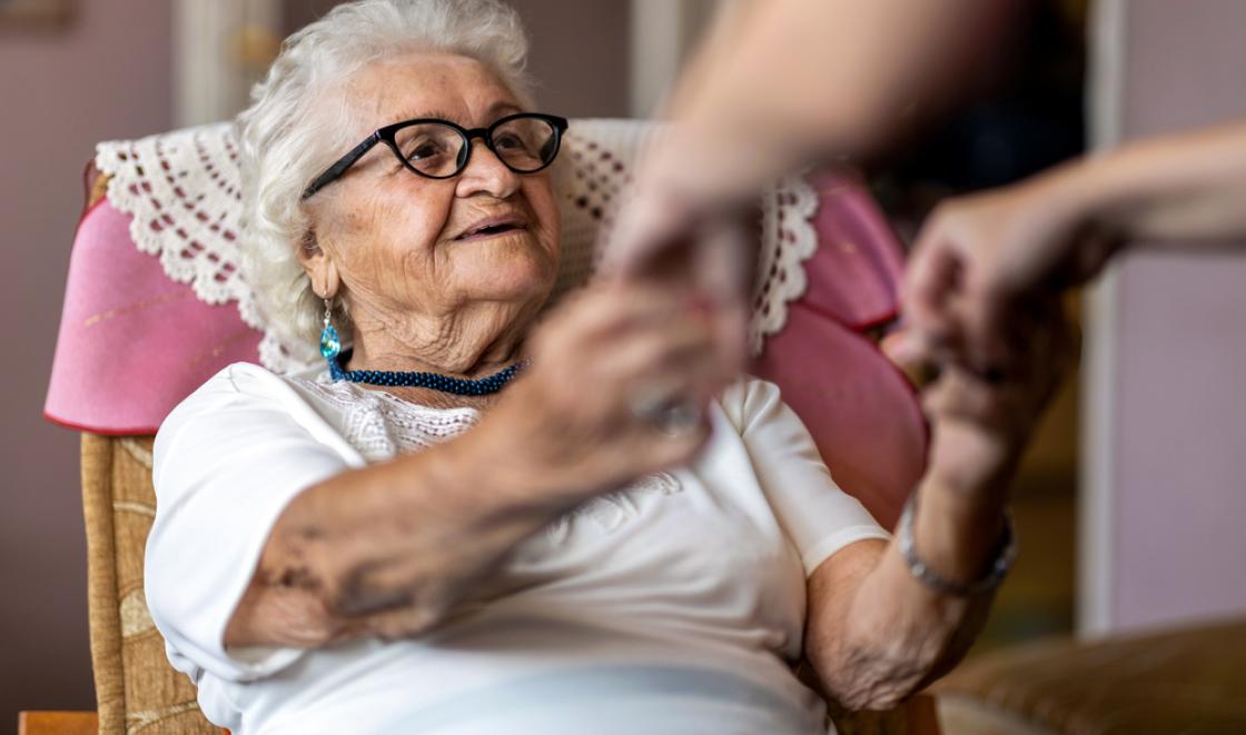 Elderly woman in chair holding hands with someone