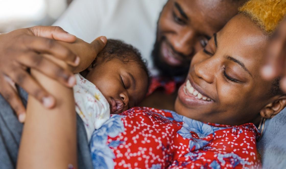 Black mother and father laying down with baby on the mother's chest. Parents are smiling down at the baby
