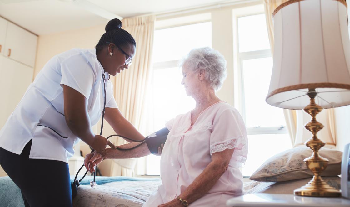 Social care assistant taking blood pressure of elderly patient